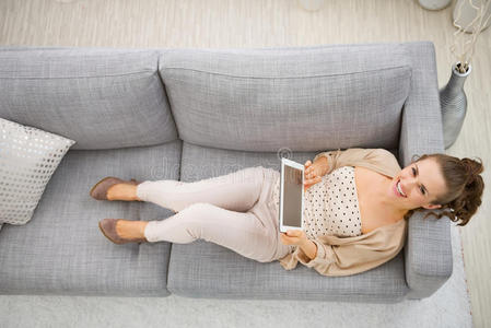 微笑的女人躺在沙发上，手里拿着平板电脑