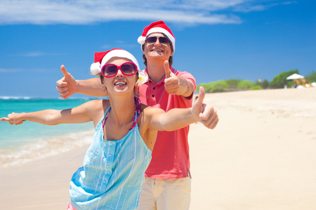 在圣诞老人的帽子笑热带海滩上的年轻夫妇。新的一年