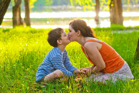 妈妈和儿子的女人和孩子坐在草在一元接吻