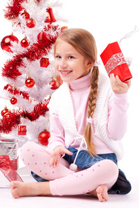 女孩坐在白色的人工圣诞树礼品与附近的地板上