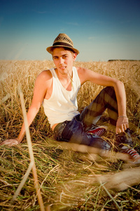 传统农村戴帽子坐小麦领域背景的年轻男子的图片