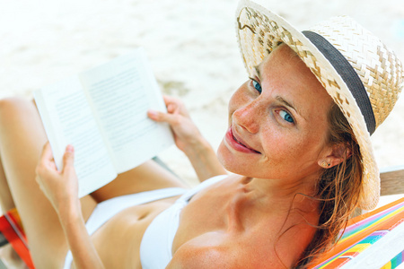 年轻漂亮的女人坐在读一本书的海滩上