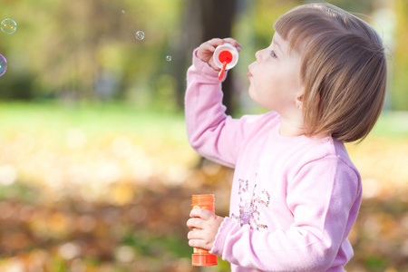 漂亮的小女孩制作泡沫鼓风机在秋天的森林