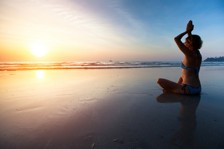瑜伽女人坐在海岸上在日落时