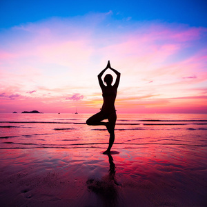 在日落时海边的年轻女子瑜伽练习