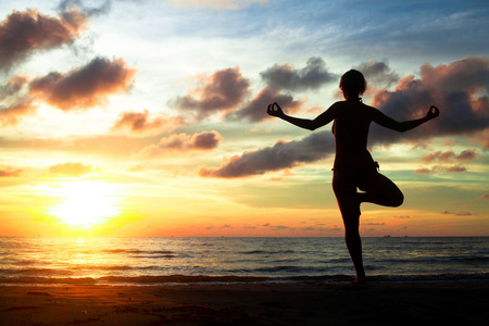 在日落期间练瑜伽在海滩上的年轻女子
