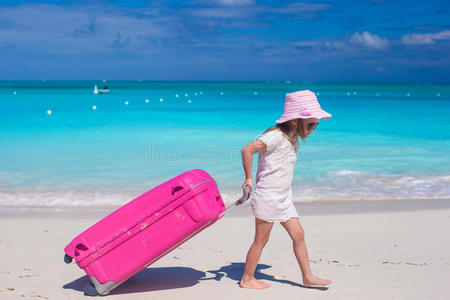 可爱的小女孩手拿着大的彩色手提箱走在热带海滩上