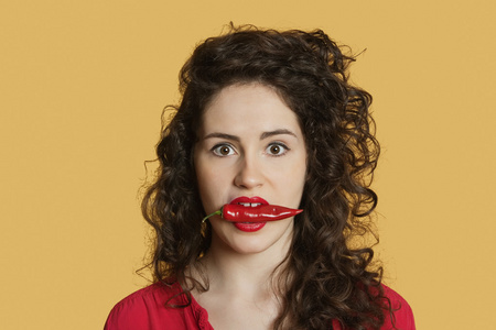 红辣椒在彩色背景在嘴里的年轻女人的肖像