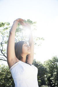 年轻的印度女人拉伸和做瑜伽在公园里的与她的手臂通过筛选的太阳