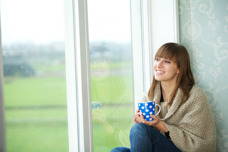 年轻女子坐在窗口与杯茶