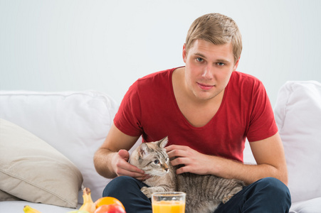男人和一只猫在家里。英俊的男人抱他在沙发上的虎斑猫