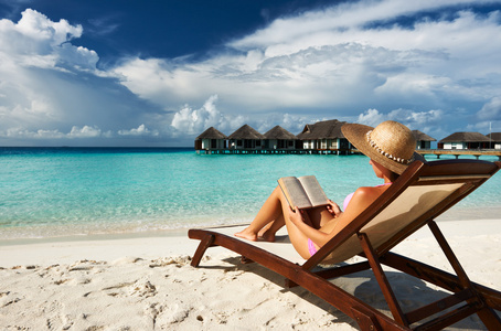 读一本书在海滩上的年轻女子