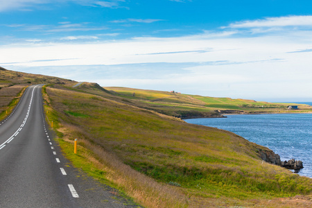 通过在蓝色夏季的天空下的冰岛景观公路