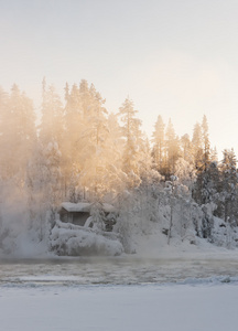 在冬天近水和薄雾森林小屋图片