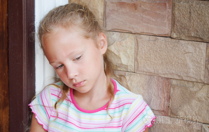 悲伤的小女孩坐在一扇门附近在金砖四国的背景