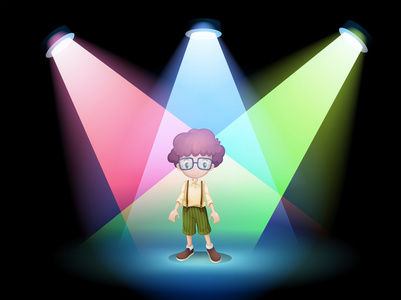 一个戴着眼镜站在聚光灯的舞台上的男孩