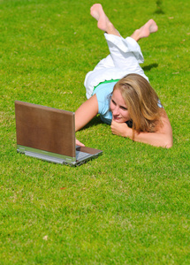 年轻的金发女人躺在草地上用的笔记本电脑