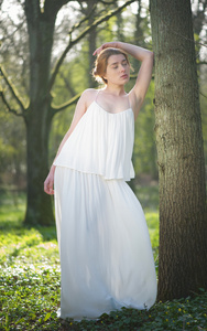 在长长的白色礼服站在森林中的优雅女人