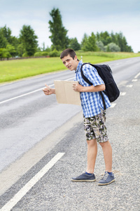 男孩搭便车等待车停在夏天的道路上