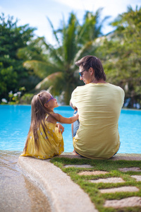 后一个年轻的父亲和他可爱的女儿坐在游泳池附近的视图
