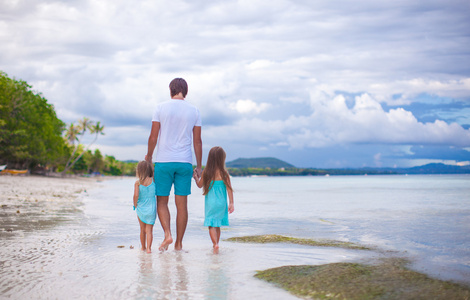 父亲和两个小女儿在海边散步的后视图