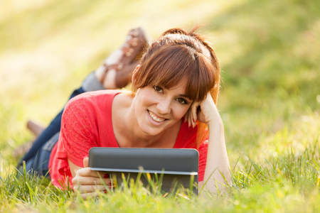 在草地上的漂亮黑发女孩正在看一个数字屏幕