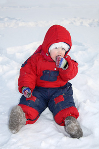 小女孩穿保暖连身衣坐在雪上和吃雪