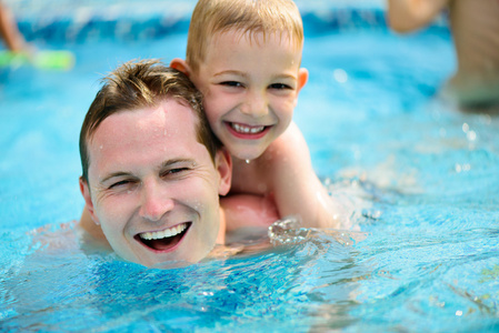 年轻爸爸和小儿子在游泳池中游泳