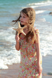 可爱快乐的小女孩，在海滩上的海星举行阳光灿烂的日子