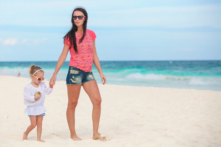 年轻漂亮的妈妈和她可爱的小女儿，白色阳光明媚的沙滩上散步