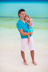 年轻爸爸和他的小女儿在热带的白色沙滩上散步