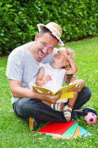 父亲同时躺在草地上，在花园里给他的女儿读一本书