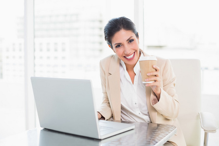 快乐的女商人在笔记本电脑上工作时喝咖啡