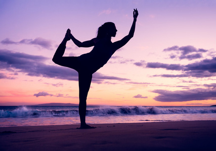 在日落时练瑜伽在海滩上的女人