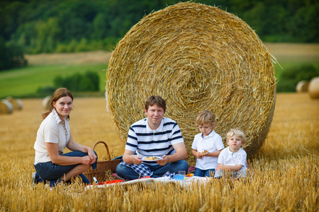 快乐的四人家庭在夏季黄色干草字段上野餐