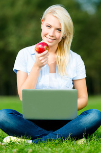 手提电脑和苹果坐在绿色的草地上的女孩
