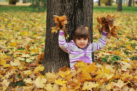 可爱的小女孩在玩树叶在秋天公园