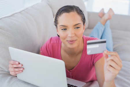 微笑的信用卡和一台笔记本电脑在沙发上的女人