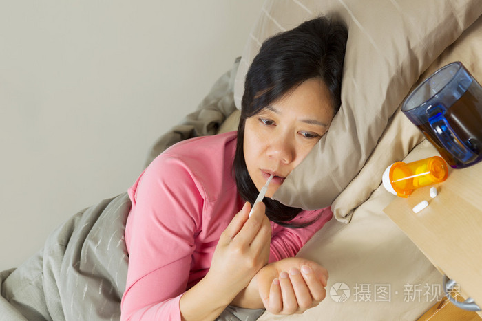 成熟的女人躺在床上生病时使用温度计