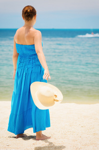 蓝裙子的女人在海滩上引发的帽子