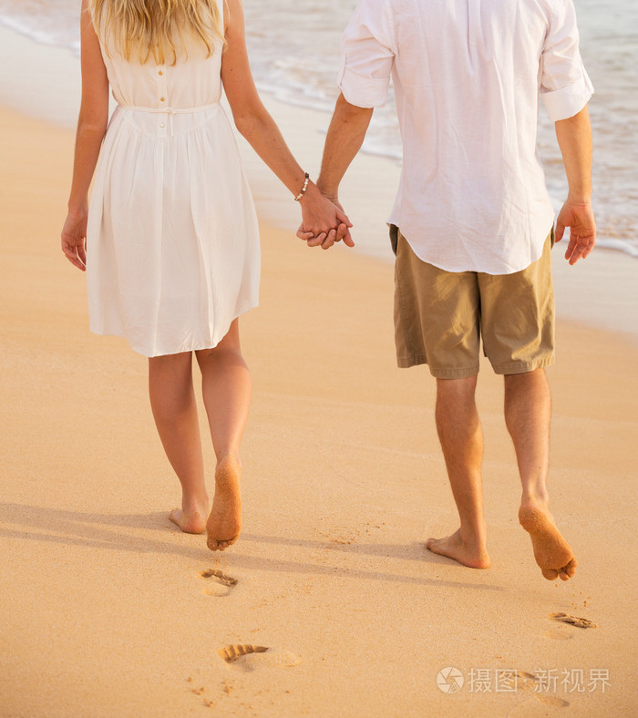 浪漫的情侣牵手在日落时分在海滩上散步男子