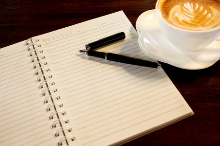 咖啡杯，螺旋笔记本和笔在木桌酒泉