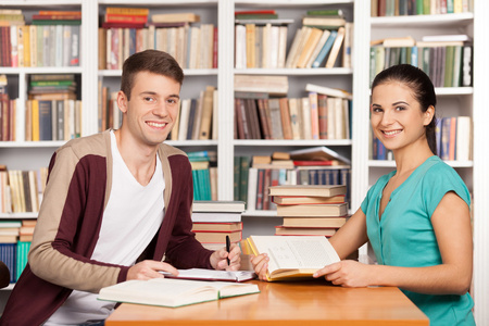 性格开朗的年轻男人和女人坐在图书馆的柜台上