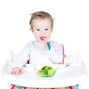 一个可爱的蹒跚学步的孩子在白色高脚椅上吃花椰菜的画像