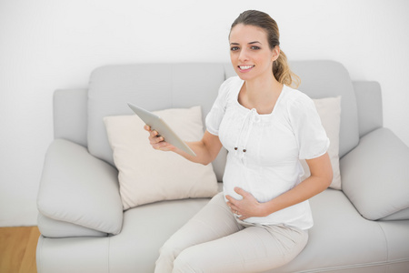 怀孕的妇女抱着她微笑着看镜头的平板电脑的内容