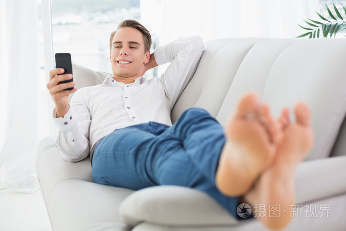 轻松的年轻男子躺在沙发上和短信