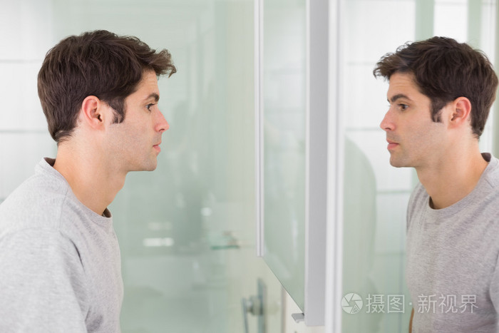 一名年轻男子微笑着自己在浴室的镜子中的侧视图