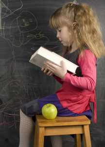 可爱的小女孩，与书和绿色的苹果，靠近黑板的肖像