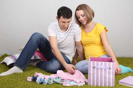 年轻孕妇和她的丈夫在家里地板上折叠婴儿服装