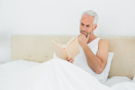 轻松成熟的男人躺在床上看书